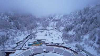 Dağlarda kış Alp Paten Pisti Medeo. Karlı ormanın ve dağların drone görüntüsü. Beyaz bulutlar ve sis vadide. Kar temizleme işlemi başladı. Büyük bir stadyum. Almaty, Kazakistan