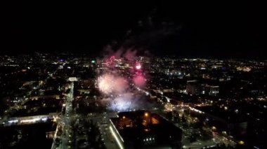 Şehir merkezindeki havai fişeklerden gelen büyük parlak ışıklar. Gece şehri Almaty 'deki bir İHA' nın hava görüntüsü, renkli ışıklar ve fenerler. İnsanlar dinleniyor. Arabalar geliyor. Şehirde bir tatil.