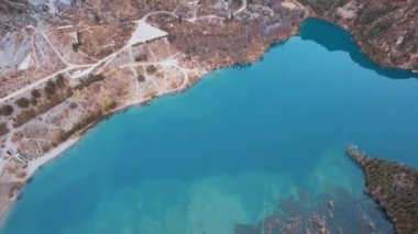 Issyk Dağı Gölü ve Baraj 'ın en üst manzarası. Küçük bir nehir göle akıyor. Tepelerde sarı-yeşil ağaçlar var. Su gökyüzünü yansıtır. İnsanlar kıyı boyunca ve patika boyunca yürür. Kazakistan