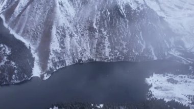 Dağdaki Kolsai Gölü 'nün üzerinde bulutların üzerinde uçuyor. Karlı dağların ve ormanın en üst manzarası. Karanlık göl suyu. Beyaz bulutlar yüzüyor. Vadideki dik kayalıklar. Kazakistan 'ın Doğası, Almaty