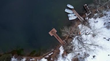 Kolsai Dağı Gölü, kış ormanında. Bulutların, kozalaklı ağaçların, aynalı suyun, kardaki tepelerin ve dağların drone görüntüsü. Beyaz tekneli bir iskele var. Temiz su. Kazakistan, Almaty