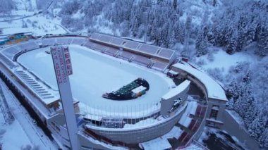 Dağlarda kış Alp Paten Pisti Medeo. Karlı ormanın ve dağların drone görüntüsü. Beyaz bulutlar ve sis vadide. Kar temizleme işlemi başladı. Büyük bir stadyum. Almaty, Kazakistan