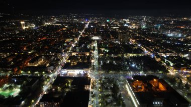 Gece şehrinde büyük bir konser. Kalabalığın insansız görüntüsü, ışınları ve ışık huzmeleri. Işıklı büyük bir bina. Arabalı yollar, yayalı sokaklar ve etrafta bir park var.