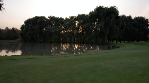 골프장에서 노을에 버드나무와 연못을 수있다 연못에 나무와 태양을 반사하는 잿빛이다 — 비디오