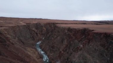 Zümrüt nehri olan bozkırdaki Büyük Kanyon. Toprakta siyah taşlı bir çatlak, nehrin yeşil rengi. Çalılıklar bazı yerlerde yetişir. Gergin turistler ve otobüsler var. Kazakistan