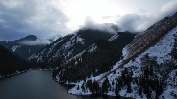 科尔赛山湖在冬季的森林里 俯瞰云彩 针叶树 倒映着平缓的水面 雪中的群山 黄昏时分船浮在一些地方 哈萨克斯坦 阿拉木图 — 图库视频影像