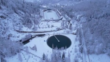 Dağlarda kış Alp Paten Pisti Medeo. Karlı ormanın ve dağların drone görüntüsü. Beyaz bulutlar ve sis vadide. Kar temizleme işlemi başladı. Büyük bir stadyum. Almaty, Kazakistan