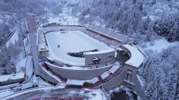 冬季高山溜冰场在山上的Medeo 鸟瞰着雪地的森林和群山 白云和浓雾笼罩着山谷 除雪工作正在进行中 一个大体育场 哈萨克斯坦阿拉木图 — 图库视频影像