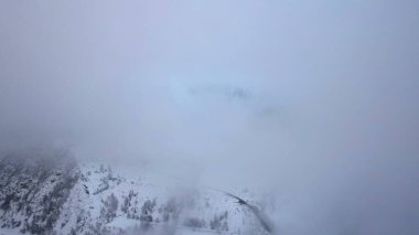 Bulutlarda kozalaklı ağaçlarla kaplı karlı dağlar. Medeo Barajı. Her şey sis ve karda. Noel ve yeni yıl geldi. Yoldaki, barajdaki ve ağaçlardaki insansız hava aracı görüntüsü. Almaty, Kazakistan