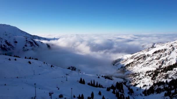 从空中俯瞰雪山和白云 贡多拉路 有小木屋人们正在滑雪板上滑行 针叶树生长 一片云雾弥漫在峡谷中 — 图库视频影像