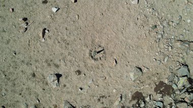 Taştan yapılmış güneş saatinin drone görüntüsü. Güneşin gölgesi saatin kaç olduğunu gösteriyor. Etrafta büyük taşlar var, yosunlar yerlerde yetişiyor. Sandy dağlarda dolaşır. Kazakistan