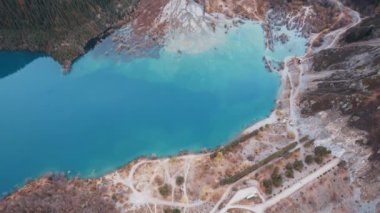 Issyk Dağı Gölü ve Baraj 'ın en üst manzarası. Küçük bir nehir göle akıyor. Tepelerde sarı-yeşil ağaçlar var. Su gökyüzünü yansıtır. İnsanlar kıyı boyunca ve patika boyunca yürür. Kazakistan