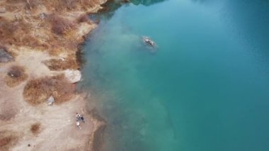 Issyk Dağı Gölü ve Baraj 'ın en üst manzarası. Küçük bir nehir göle akıyor. Tepelerde sarı-yeşil ağaçlar var. Su gökyüzünü yansıtır. İnsanlar kıyı boyunca ve patika boyunca yürür. Kazakistan
