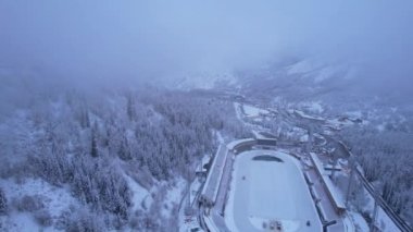 Dağlarda kış Alp Paten Pisti Medeo. Karlı ormanın ve dağların drone görüntüsü. Beyaz bulutlar ve sis vadide. Kar temizleme işlemi başladı. Büyük bir stadyum. Almaty, Kazakistan