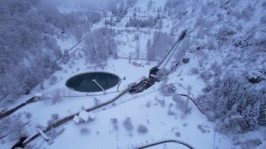 Almaty 'de kozalaklı ağaçlarla kaplı karlı dağlar. Dağ suyu için bir rezervuar. Medeo Barajı ve sağlık merdivenleri. Her şey bulutlar ve karla kaplı. İnsanlar ve teleferik görünüyor.