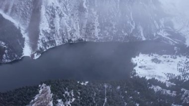 Dağdaki Kolsai Gölü 'nün üzerinde bulutların üzerinde uçuyor. Karlı dağların ve ormanın en üst manzarası. Karanlık göl suyu. Beyaz bulutlar yüzüyor. Vadideki dik kayalıklar. Kazakistan 'ın Doğası, Almaty