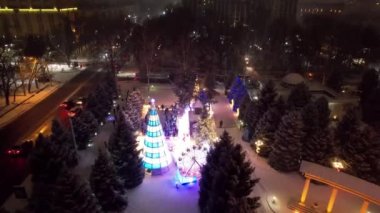 Noel ağacıyla süslenmiş parlak Noel süslemeleri. Noel ağacında çelenkler ve neon oyuncaklar parlıyor. Noel ve Yeni Yıl için dekorasyon. Kar yağıyor. İnsanlar fotoğraf çeker. İHA 'dan üst görünüm
