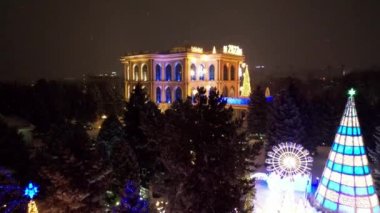 Noel ve yeni yıl için çok güzel dekore edilmiş bir ev. Kar yağıyor, Noel ağaçlarındaki çelenkler parlıyor, bir atlıkarınca, çeşitli dekorasyonlar, toplar ve oyuncaklar. İnsanlar yürüyor. Üst Manzara. Almaty