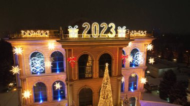 Noel ve yeni yıl için çok güzel dekore edilmiş bir ev. Kar yağıyor, Noel ağaçlarındaki çelenkler parlıyor, bir atlıkarınca, çeşitli dekorasyonlar, toplar ve oyuncaklar. İnsanlar yürüyor. Üst Manzara. Almaty