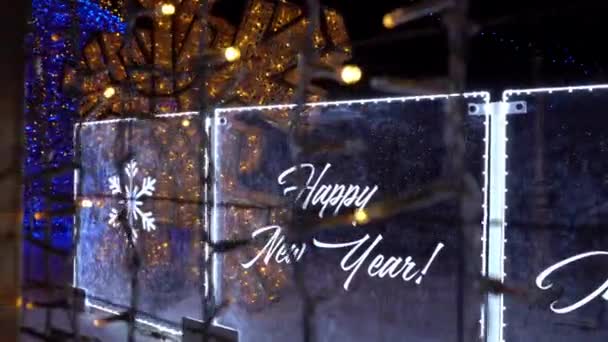 尼昂语新年快乐 有三种语言 篱笆上的花环闪闪发光 新年和圣诞装饰品 玩具和圣诞树 白色的雪花正在落下 阿拉木图 — 图库视频影像