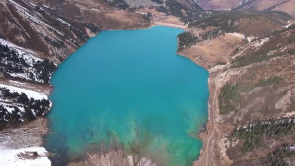 ターコイズブルーの水を持つ山の中の湖 澄んだ水 針葉樹と雪の山のドローンビュー 人々は海岸に沿って歩くと 低茂みが成長します 大きなアルマトイ湖 カザフスタン — ストック動画