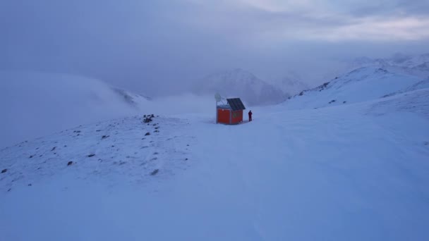 云中的高山上的一个救援小屋 有一个登山者站在房子旁边 白云笼罩着雪山 黄色的黎明和乌云 2023阿拉木图 — 图库视频影像