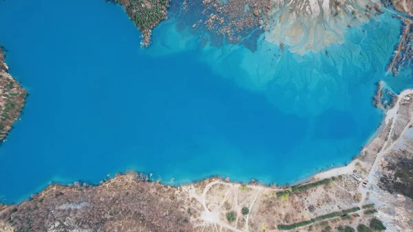 Top view of the turquoise water of a mountain lake. Clean clear water with streaks on the bottom. Patterns from a mountain river. The color shimmers from blue-green to blue. Trees in the water. Issyk