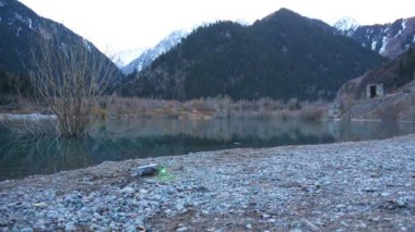 Quadcopter bir dağ gölünün sahilinden havalanıyor. Küçük gri bir dron bıçaklarını fırlatır, yeşil-kırmızı ışıklarla parıldar ve tepeden yükselir. Sandy ve Rocky plajı. Uzakta bir orman