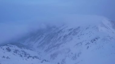 Karlı dağlarda bulutların olduğu mistik şafak. Beyaz tepeler bulutlar ve karla kaplıdır. Dik kayalıklar. Zirvenin zirveleri. Şafak vakti güneş ışınları bulutların arasından geçer.