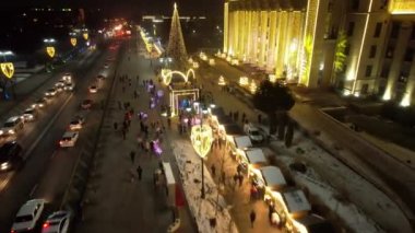 A large Christmas tree in the lights on the square. Top view from the drone on the street with cars and people, a bright building in garlands, various decorations for the new year. Almaty, December