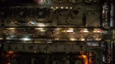 Red big trucks with Coca Cola drive through the streets of the city. Average traffic of cars. Lights and headlights are shining. New Years mood. Top view from the drone on the houses and the road