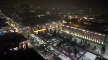 A large Christmas tree in the lights on the square. Top view from the drone on the street with cars and people, a bright building in garlands, various decorations for the new year. Almaty, December