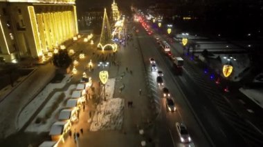 A large Christmas tree in the lights on the square. Top view from the drone on the street with cars and people, a bright building in garlands, various decorations for the new year. Almaty, December