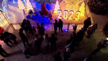 Noel ağacıyla süslenmiş parlak Noel süslemeleri. Noel ağacında çelenkler ve neon oyuncaklar parlıyor. Noel ve Yeni Yıl için dekorasyon. Kar yağıyor. İnsanlar fotoğraf çeker. İHA 'dan üst görünüm