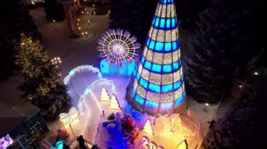 Noel ve yeni yıl için çok güzel dekore edilmiş bir ev. Kar yağıyor, Noel ağaçlarındaki çelenkler parlıyor, bir atlıkarınca, çeşitli dekorasyonlar, toplar ve oyuncaklar. İnsanlar yürüyor. Üst Manzara. Almaty