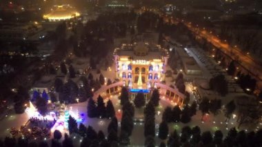 Noel ve yeni yıl için çok güzel dekore edilmiş bir ev. Kar yağıyor, Noel ağaçlarındaki çelenkler parlıyor, bir atlıkarınca, çeşitli dekorasyonlar, toplar ve oyuncaklar. İnsanlar yürüyor. Üst Manzara. Almaty