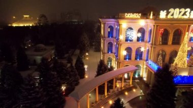 Noel ve yeni yıl için çok güzel dekore edilmiş bir ev. Kar yağıyor, Noel ağaçlarındaki çelenkler parlıyor, bir atlıkarınca, çeşitli dekorasyonlar, toplar ve oyuncaklar. İnsanlar yürüyor. Üst Manzara. Almaty