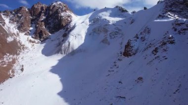 Dağlarda eski bir kar buzulu. Yukarıdan, karla kaplı dik uçurumlardaki bir dronun görüntüsü. Bir buzulla kaplı yüksek zirveler. Bazı yerlerde büyük taşlar var. İzler görünüyor.
