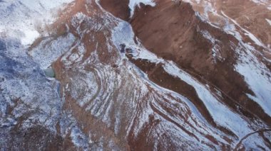 High snowy peaks and a small glaciological station. Drone view of the blue sky with clouds, steep cliffs and rocks. An ancient glacier covered with snow. Small houses are standing. Moraine lake