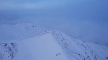 Karlı dağlarda bulutların olduğu mistik şafak. Beyaz tepeler bulutlar ve karla kaplıdır. Dik kayalıklar. Zirvenin zirveleri. Şafak vakti güneş ışınları bulutların arasından geçer.