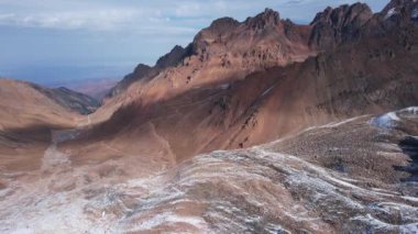 Top view of the high rocky mountains with trails. In places there is snow and yellow-orange plants grow. Shadows from clouds float on the rocks. A place to climb to the top. The mountains of Almaty