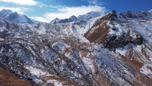 高山中的一座古老的雪冰川 山顶上覆盖着雪 在一些地方有陡峭的悬崖和巨大的岩石 蓝天白云 无人机的俯瞰 — 图库视频影像