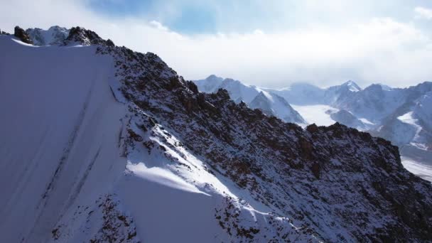 高山中的一座古老的雪冰川 山顶上覆盖着雪 在一些地方有陡峭的悬崖和巨大的岩石 蓝天白云 无人机的俯瞰 — 图库视频影像