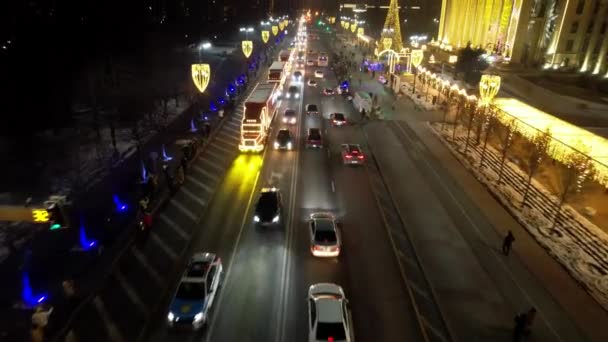 一辆可口可乐汽车组成的新年大篷车正在沿路行驶 人们相遇并挥手 在花环里有一棵高大的圣诞树 灯光和装饰品四处闪烁着 Almaty 2022 — 图库视频影像