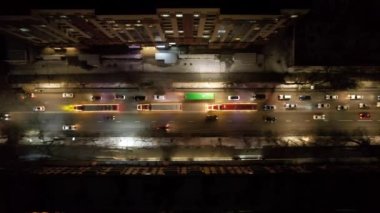 Red big trucks with Coca Cola drive through the streets of the city. Average traffic of cars. Lights and headlights are shining. New Years mood. Top view from the drone on the houses and the road
