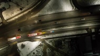 Red big trucks with Coca Cola drive through the streets of the city. Average traffic of cars. Lights and headlights are shining. New Years mood. Top view from the drone on the houses and the road