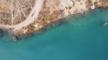 Dağ gölündeki suyun koyu mavi ayna rengi. Düz yüzey bir ayna gibidir, ağaçlar, sarı-yeşil tepeler, dağlar ve gökyüzü yansıtılır. Ağaç gövdeleri suda duruyor. Issyk