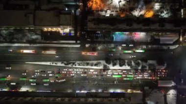 Red big trucks with Coca Cola drive through the streets of the city. Average traffic of cars. Lights and headlights are shining. New Years mood. Top view from the drone on the houses and the road