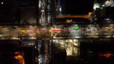 Red big trucks with Coca Cola drive through the streets of the city. Average traffic of cars. Lights and headlights are shining. New Years mood. Top view from the drone on the houses and the road