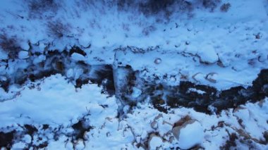 Ormanda karlı bir nehir yatağı boyunca akan bir dağ nehri. Büyük taşlar var. Yukarıdan bak. Hayvan izleri bazı yerlerde görülebilir. Nehir boyunca bir inşaat var, beton bir duvar.